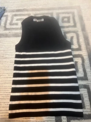 Randig ärmlös topp från Zara - Snygg ärmlös topp från Zara i svart och vitt med breda horisontella ränder. Toppen är ribbstickad och har en rak passform som ger en stilren look. Perfekt att matcha med jeans eller kjol för en trendig outfit.