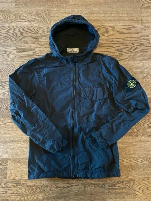 Stone Island Vindjacka - Stone Island vindjacka. Mörkblå/svart, i Storlek S. Sparsamt använd, i jättefint skick. QR-kod för äkthets-verifiering tillgänglig. Säljs pga minskad användning. Bara att höra av dig vid intresse, frågor eller önskan om fler bilder! Mvh