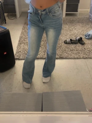 Ljusblå bootcut jeans - Säljer ett par ljusblå bootcut jeans med klassisk femficksdesign och hög midja. Jeansen har en snygg tvätt med slitningar framtill och lätt utsvängda ben. Perfekta för en trendig och avslappnad look.