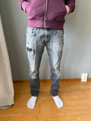 Replay ambass (snygg slitning och fade) - Säljer ett par grå jeans med slitningar och hål på låret och vid fickorna. Jeansen har en smal passform och klassisk femficksdesign. Perfekta för en avslappnad och trendig stil.