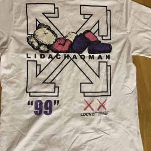 Vit t-shirt från Off-White - Säljer en vit t-shirt från Off-White med tryck på både fram- och baksidan. Framsidan har texten 'OFF' och två rosa kryss. Baksidan har ett stort grafiskt tryck med texten 'LIDACHAOMAN' och '99'.