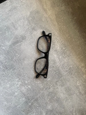 Chrome hearts glassögon  - Snygga svarta glasögon med rektangulära bågar och små vita blommor i hörnen. Bågarna är i plast och har en klassisk form som passar till många stilar. Perfekt accessoar för dig som vill sticka ut lite extra. Helt nya  ingen låda