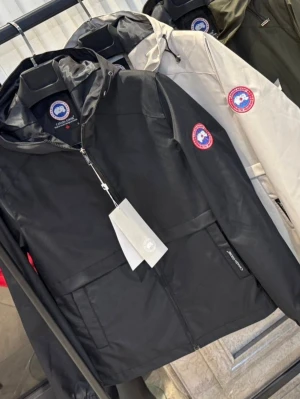 Svart vindjacka från Canada Goose - Snygg svart vindjacka från Canada Goose med huva och dragkedja framtill. Jackan har en klassisk logotyp på ärmen och praktiska fickor. Perfekt för blåsiga dagar och enkel att matcha med olika outfits.