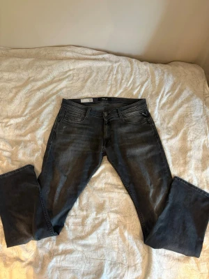 Mörkgrå jeans från Replay - Snygga mörkgrå jeans från Replay med klassisk femficksdesign och diskreta slitningar. Jeansen har raka ben och normal midja, tillverkade i mjuk bomullsdenim med lite stretch för extra komfort.