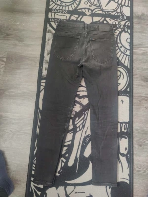 Svarta skinny jeans från Lee - Säljer ett par svarta skinny jeans från Lee med klassisk femficksdesign och smal passform. Jeansen har en diskret Lee-logga på bakfickan och är tillverkade i stretchigt denimtyg för extra komfort. Perfekta för en stilren och avslappnad look.