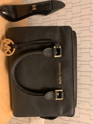 Svart handväska MK - svart handväska från MK. Klassisk modell som passar lika bra till vardag som till jobb eller finare tillfällen. Väskan är begagnad och har fläckar på insidan och saknar bandet, vilket tydligt syns på bilderna. Inte Äkta. 