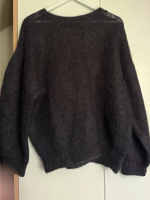 Mörkgrå/svart fluffig stickad tröja ( M/L ) - Mysig mörkgrå stickad tröja med fluffig känsla och avslappnad passform. Tröjan har rund halsringning och långa ärmar, perfekt för lager på lager. Materialet ser ut att vara en mjuk mohair- eller ullblandning.