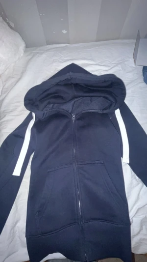 Mörkblå hoodie från russemerch - Snygg mörkblå hoodie med vit dragsko och dragkedja framtill. Modellen har huva och två stora fickor på magen. Perfekt för en chill och avslappnad stil. Materialet känns mjukt och bekvämt mot huden. Har använt den 3 gånger bara!