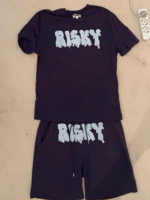  Risky sett - Säljer ett mörkblått set från Risky med matchande t-shirt och shorts. Båda plaggen har ett stort ljusblått tryck med texten 'RISKY' i en cool, droppande stil. Setet är gjort i mjukt bomullsmaterial och har avslappnad passform. Perfekt för en chill och trendig look.