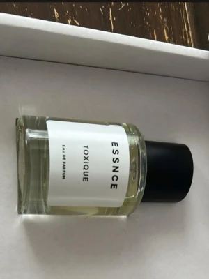 ESSNCE Toxique Eau de Parfum - ESSNCE Toxique Eau de Parfum kommer i en stilren, genomskinlig glasflaska med svart lock och vit etikett. Parfymen har en minimalistisk design som känns modern och fräsch. 