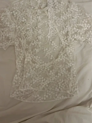 Vit blommig meshblus med puffärm - En jättesöt vit mesh blus med spets och en snygg öppen rygg. Toppen är i fint skick från NAKD i storlek 36/S