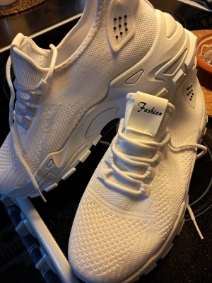 Vita sneakers med stickad ovandel - Snygga helvita sneakers med stickad ovandel och robust sula. Skorna har ventilerande meshdetaljer och klassisk snörning. Perfekta för dig som gillar en clean och sportig look. Märket 'Fashion' syns på plösen.