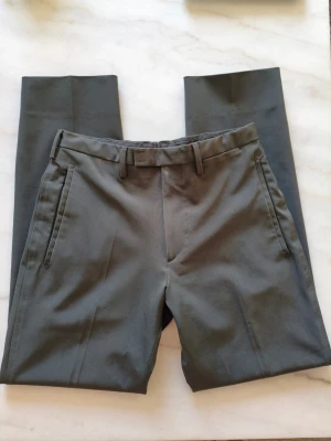 Prada Technostretch byxor - Säljer ett exklusivt par Prada Technostretch byxor i perfekt skick! Dessa byxor kombinerar lyx, komfort och stil i en fantastisk design.Storlek: 44 Slim Fit 70 cm i omkrets och 95 cm långa. Färg: Antracit en elegant mörkgrå färg. Gjorda av 90% polyester 10% spandex.Materialet känns mjukt och har en lätt stretch för extra komfort.
