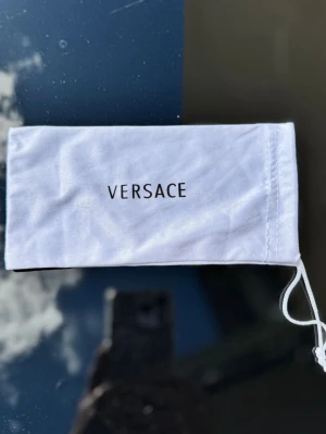 Vit påse till glasögon / accessoarer - Vit påse i mjukt tyg, perfekt för att förvara solglasögon eller andra små accessoarer. Påsen har dragsko och stilren svart logga framtill.