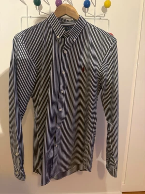 Randig skjorta från Polo Ralph Lauren - Snygg blåvit randig skjorta från Polo Ralph Lauren i slim fit-modell. Skjortan har långa ärmar, klassisk krage och knäppning framtill. Broderad logga på bröstet. Perfekt för en stilren look.