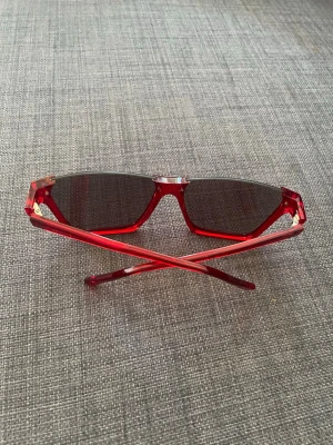 Celine Röda sportiga solglasögon - Snygga solglasögon med röd, transparent båge och mörka rektangulära glas. Glasögonen har en sportig och modern design med markerade kanter och lätta plastskalmar. Perfekta för dig som vill sticka ut med en cool accessoar.