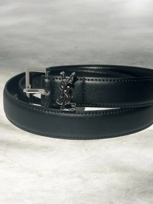 Svart skärp från Saint Laurent - Stilrent svart skärp från Saint Laurent i skinn med klassiskt silverfärgat YSL-spänne. Perfekt accessoar för att lyfta din outfit med en lyxig touch. Skärpet har en enkel design med diskreta sömmar och metallspänne.