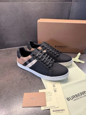 Burberry sneakers med klassiskt rutmönster - Snygga sneakers från Burberry med svart läder framtill och klassiskt beige rutmönster på sidorna. Skorna har vita sulor och svarta detaljer vid hälen samt Burberry-logga bak. Perfekta för dig som gillar stilrena och exklusiva sneakers.