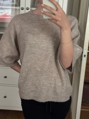 Beige stickad tröja från 157 - Beige stickad tröja från 157 med rund halsringning och avslappnad passform. Tröjan har halvlånga ärmar. 