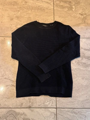Svart stickad tröja Jack & Jones - Snygg svart stickad tröja från Jack & Jones med rund halsringning och ribbade muddar. Perfekt för lager-på-lager och enkel att matcha med jeans eller chinos. Klassisk modell med diskret struktur i materialet.