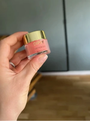 DIPSY Dip Powder Caramel Appel - DIPSY Dip Powder i färgen Caramel Appel, en snygg karamellrosa nyans. Kommer i en liten glasburk med guldfärgat lock. Perfekt för dig som vill ha ett trendigt och hållbart nagellackspulver till dina naglar.