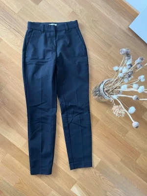 Svarta kostymbyxor med pressveck - Snygga svarta kostymbyxor med raka ben och pressveck. Byxorna har hällor för skärp, sidfickor och två bakfickor. Perfekta för en stilren look. Materialet ser ut att vara en blandning av polyester och bomull.