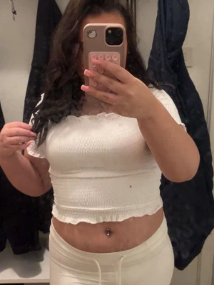 Vit croppad offshoulder topp - Säljer en söt vit croppad topp med offshoulder och smockad design. Toppen har korta ärmar och volangkant vid halsringning och nederkant. Perfekt för dig som gillar en trendig och feminin stil.( finns en liten fläck syns knappast) 