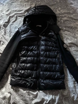 Moncler Cardigan  - Svart äkta moncler cardigan med avtagbar luva. Jackan är varsamt använd. Enda defekten på jackan är en knapp har lossnat därav priset. Jackan passar både tjej och kille. Kan ta emot bud🤍