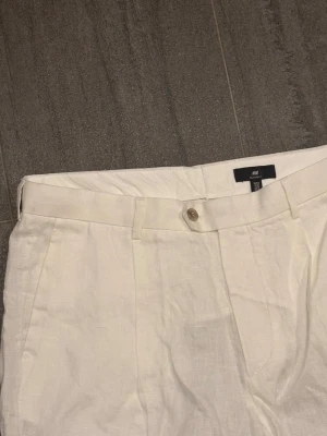 Vita linnebyxor från H&M - Snygga vita linnebyxor från H&M med raka ben och klassisk passform. Byxorna har hällor för bälte, knappstängning och sidfickor. Perfekta för en avslappnad och stilren look under varma dagar.