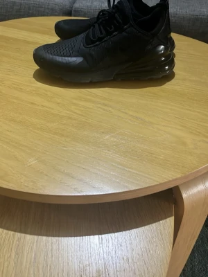 Svarta Nike Air Max 270 sneakers - Säljer ett par helsvarta Nike Air Max 270 sneakers med synlig luftbubbla i hälen och ventilerande mesh-ovandel. Skorna har en sportig look med klassisk Nike-logga på sidan och snörning framtill. Perfekta för dig som gillar streetwear och bekväma skor.  Priset går att diskuteras 