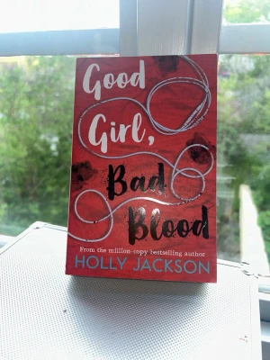 Good Girl, Bad Blood av Holly Jackson - En spännande skönlitterär bok med röd och svart framsida, skriven av Holly Jackson. Omslaget har vita och svarta slingrande hörlurar och text i vitt, svart och blått. Perfekt för dig som gillar true crime och mysterier.