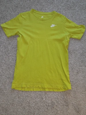 Gulgrön Nike t-shirt i bomull, Size 147-158 cm - Nike t-shirt i en fräsch gulgrön färg med klassisk vit logga på bröstet. Modellen är enkel med rund hals och korta ärmar, perfekt för en avslappnad stil. Tillverkad i mjuk bomull som känns skön mot huden. Storlek är 147-158 cm. Meddela mig så tidigt som möjligt om du vill ha den! 💫 (Prissänkning kan ske)