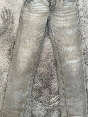 Grå Jack and Jones jeans med slim fit passform, bakfickor - Snygga grå jeans med slim fit passform och klassiska bakfickor med dekorativa sömmar. Jeansen har en ljus tvätt och small midja. Perfekta för en slim fit och trendig stil.