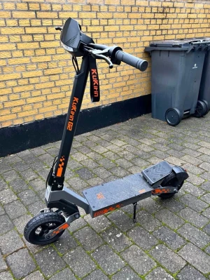 Svart el-scooter Kukirin G2 - Elektrisk scooter från Kukirin, modell G2, i svart med orange detaljer. Scootern har bred fotplatta, robusta däck och handtag med bra grepp. Perfekt för att ta sig fram snabbt i stan. Tillverkad i metall och plast.