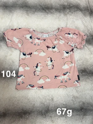 Rosa t-shirt med enhörningar - Supersöt rosa t-shirt från polarn o pyret med korta ärmar och gulligt enhörningsmönster, regnbågar och moln. Perfekt för dig som gillar färgglada och lekfulla plagg. 🌸 Fint använt skick. Storlek 104