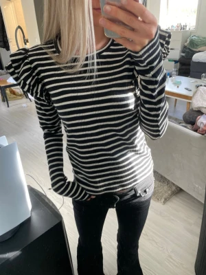 Randig topp med volangaxlar - Snygg svartvit randig topp med långa ärmar och volangdetaljer på axlarna, ribbad. Bra skick och från Zara💕