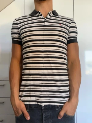 Randig pikétröja från J.Lindberg - Svart och vit randig piké från J.Lindberg. Strl S. Inga defekter. Modellen är 178 cm och väger 77 kg. Hör gärna av dig vid frågor!
