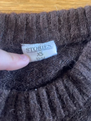Brun stickad tröja från Stories XS - Mysig brun stickad tröja från Stories i storlek XS. Tröjan har en klassisk rund halsringning, långa ärmar och ribbstickade muddar vid ärmslut och nederkant. Perfekt för lager-på-lager och enkel att matcha med jeans eller kjol. Skulle kunna möta upp och lämna 💛