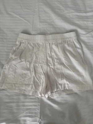 Vita linne-shorts med resårmidja - Säljer ett par vita shorts i linne med avslappnad passform och elastisk midja. 