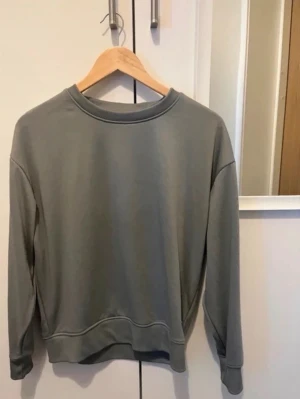 Grå sweatshirt med rund hals - En stilren grå sweatshirt med rund halsringning och långa ärmar. Tröjan har ribbade muddar vid ärmslut och nederkant, vilket ger en avslappnad och trendig look. Perfekt att matcha med jeans eller kjol för en casual stil.