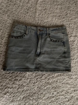Blå jeanskjol med nitar - Snygg blå jeanskjol i kort modell med coola nitar vid fickorna fram och bak. Kjolen har klassisk femficksdesign och stängs med knapp och dragkedja. Perfekt nu till sommaren! 💞