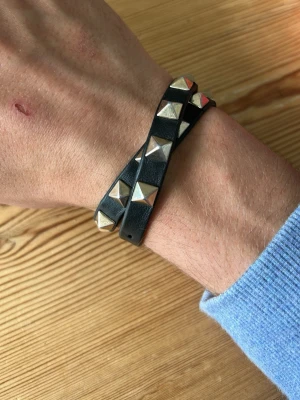 Valentino armband - Snyggt svart valentino armband i läder som lindas två varv runt handleden. Armbandet har guld pyramidformade nitar och ett spänne i metall. Riktigt snyggt och passar till allt! 