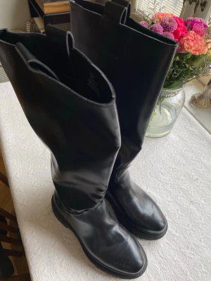 Svarta höga läderstövlar - Snygga svarta stövlar i slätt läder med högt skaft och rundad tå. Klassisk modell med dragflikar upptill för enkel påtagning. 
