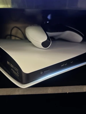 PlayStation 5 med DualSense-kontroll - Säljer en PlayStation 5 konsol från Sony tillsammans med en vit och svart DualSense-kontroll. Konsolen har en futuristisk design med rundade kanter och matta vita paneler. Perfekt för gaming och streaming. Kontrollern har inbyggd touchpad och adaptiva triggers.