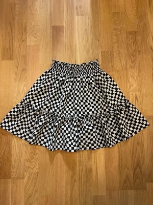 Svartvit rutig kjol från H&M - Säljer en svartvit rutig kortkjol från H&M med elastisk midja och volangdetalj. Är i barnstorlek 146/152 men sitter bra på mig som är 167cm och brukar ha vuxenstorlekar i S-XXS.