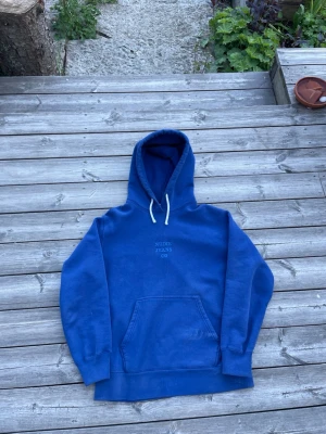 Blå hoodie från Nudie Jeans Co - Snygg blå hoodie från Nudie Jeans Co med broderad logga på bröstet. Klassisk känguruficka framtill och vita dragsnören i huvan. Tillverkad i mjuk bomull, perfekt för en avslappnad stil.