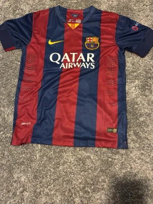 FC Barcelona Messi matchtröja - Säljer en officiell FC Barcelona matchtröja från Nike med Messi 10 på ryggen. Tröjan har breda blå och röda ränder, klubbmärke och Qatar Airways-logga framtill samt Champions League-märke på ärmen. Tillverkad i Dri-FIT-material för bästa komfort. 