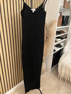 Svart långklänning med smala axelband - En svart långklänning med smala axelband och lätt strukturerat tyg. Klänningen har en rak passform och är ärmlös, perfekt för en stilren look. Märket är H&M och materialet känns som polyester. Skriv om ni vill ha bild på 🫶🏼🫶🏼