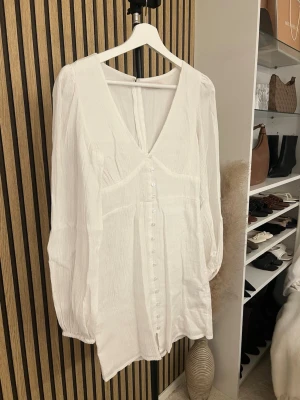 Vit omlottklänning med knappar - Superfin vit klänning med v-ringning och långa ärmar. Klänningen har knappar framtill och är tillverkad i ett lätt, krinklat material som ger en avslappnad känsla. Perfekt för sommarens alla tillfällen. Använd en gång under midsommar, nypris 599kr💕 Skriv om ni vill ha bild på 🫶🏼🫶🏼