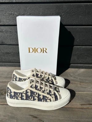 Dior Oblique låga sneakers - Snygga låga sneakers från Dior med klassiskt blått och vitt Oblique-mönster. Skorna har vita snören, gummisula med stjärndetalj undertill och tydlig Dior-logga på sidan. Ovandelen är i textil och sulan i slitstarkt gummi. Perfekta för dig som gillar exklusiv streetstyle.